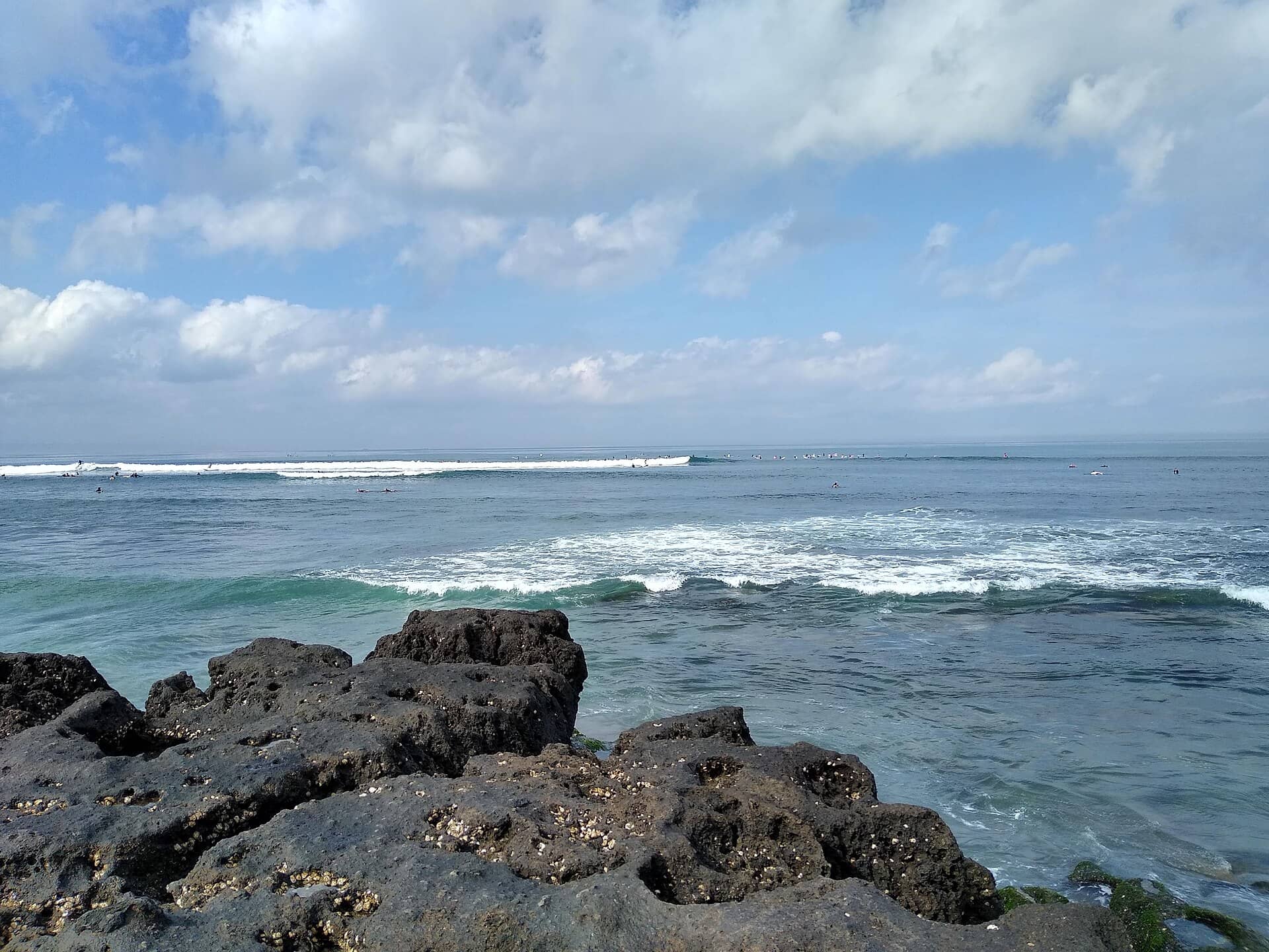 Surf lines rolling over dark volcanic rock at Canggu beach, Bali