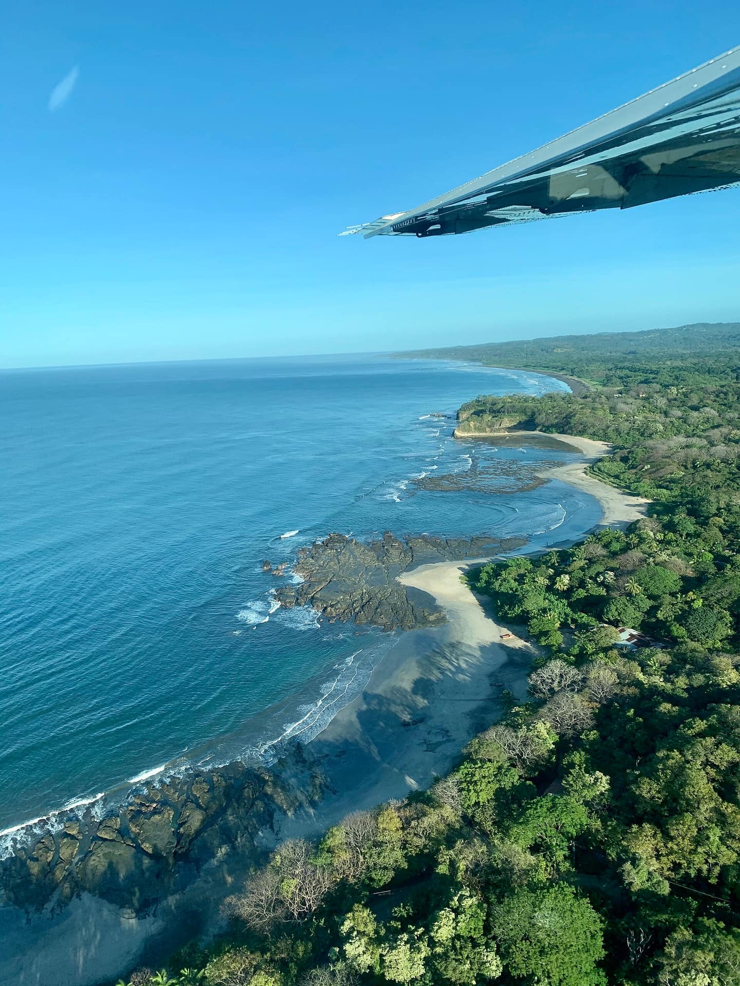 The forest-backed curve of Playa Guiones meeting Pacific swell at Nosara, seen from a light aircraft